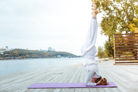 Standing on the head. Young woman standing on the head while doing outdoor exercises on the yoga carpetの写真素材