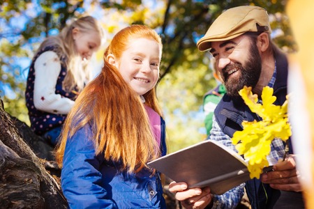 Positive mood. Cheerful red haired girl smiling to you while standing near her teacherの写真素材