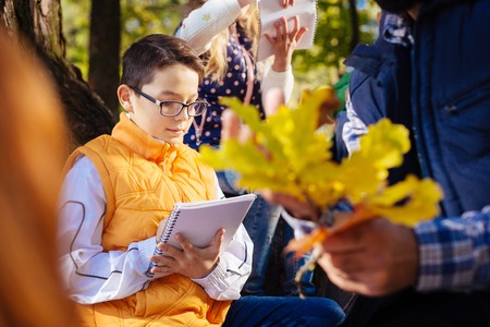 Not to forget. Smart intelligent boy writing in the notebook while being in the forest with his classの写真素材
