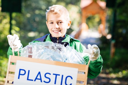 Box for plastic. Cheerful blonde boy smiling to you while holding a box with plastic bottlesの写真素材