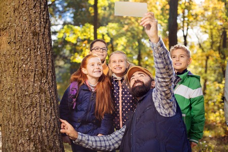 Now smile. Nice bearded man holding a digital device while taking photos with childrenの写真素材