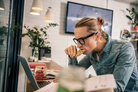 What is this. Serious young man eating his cookie while looking into the screenの写真素材