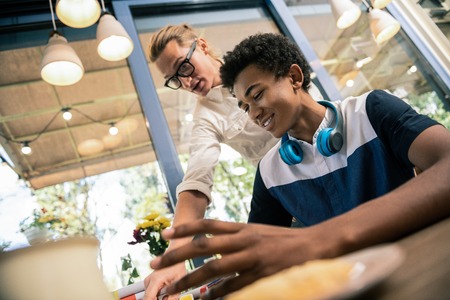 Professional tutor. Smart young man standing behind his pupil while looking at him doing the taskの写真素材