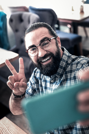 Cheerful man. Cheerful handsome dark-eyed man feeling very excited and emotional making selfieの写真素材