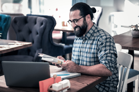 Two books. Dark-haired bearded smart teacher wearing glasses and squared shirt holding two booksの写真素材