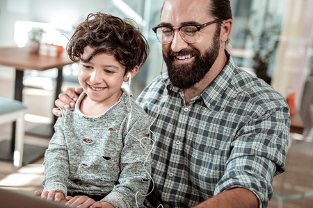 Movie on laptop. Beaming happy father and son watching movie on laptop while sharing earphonesの写真素材