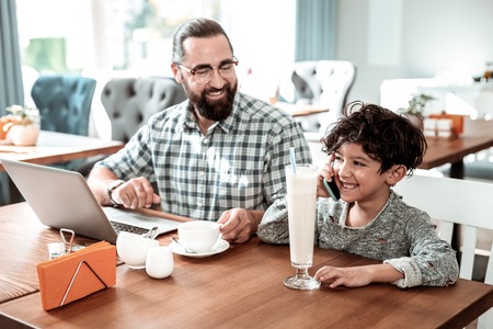 Speak by phone. Beaming little cute son speaking by phone with mother standing near fatherの写真素材