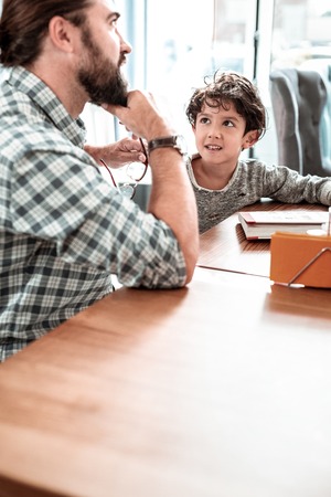 Day together. Bearded dad and cute son feeling happy spending day together sitting in restaurantの写真素材