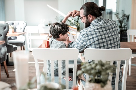 After studying. Dark-haired father wearing glasses and handsome little son feeling amazing after studying togetherの写真素材