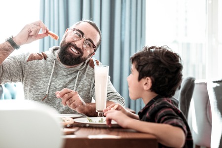 One more. Beaming dark-haired son feeling excited while taking one more piece of pizzaの写真素材