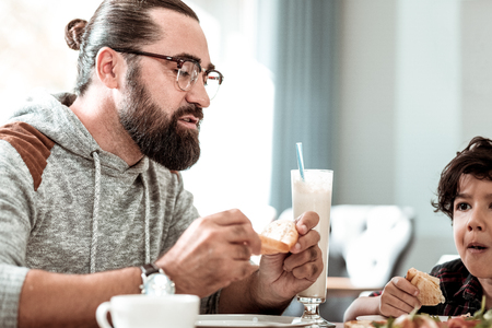 Piece of bacon. Beaming cute dark-haired boy feeling excited while eating piece of baconの写真素材