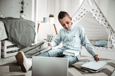 My school task. Sad cheerless boy sitting on the floor while taking his notebook from the bagの写真素材