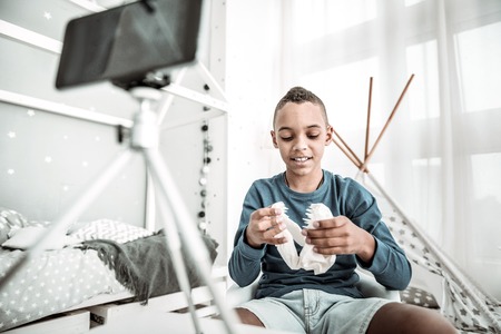 So interesting. Cheerful smart boy sitting on his bed while playing with a dinosaur skull modelの写真素材