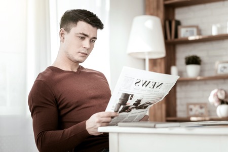 Daily news. Attentive brunette male doing press review, sitting in semi positionの写真素材