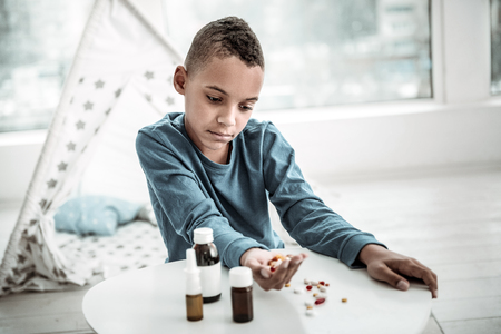 Unpleasant illness. Sad depressed boy looking at the pills while having problems with healthの写真素材