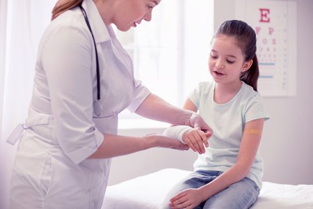 Broken arm. Dark-haired little girl wearing jeans and blue shirt coming to doctor after breaking her armの写真素材