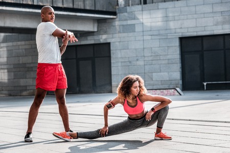 Sportive couple. Pleasant young woman doing an exercise while working out with her boyfriendの写真素材