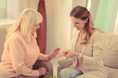 Great news. Delighted elderly woman looking at her daughters ring while being happy for herの写真素材