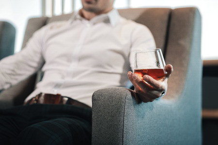 Glass of whisky. Close up of young stylish man wearing squared trousers drinking glass of whisky
