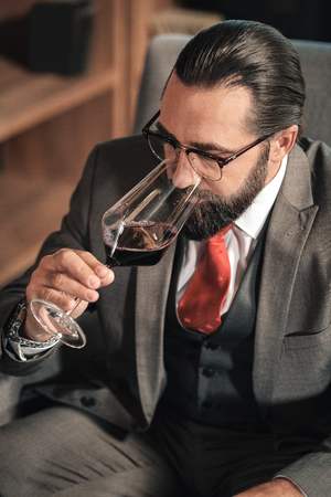 Drinking wine. Top view of stylish mature businessman drinking some red wine after working dayの写真素材
