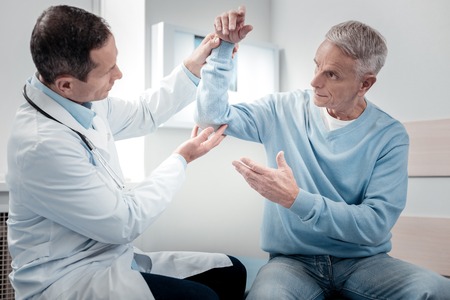 Take it higher. Serious physician looking at his patient while examining elbowの写真素材