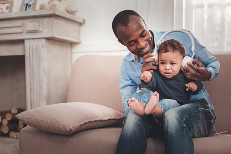 Do you like. Delighted positive man holding his baby while giving him to listen to the songの写真素材
