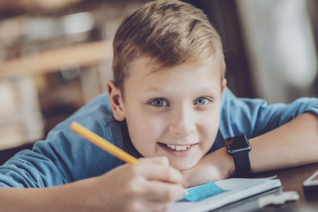 Joyful blonde child expressing positivity while doing homework with pleasureの写真素材