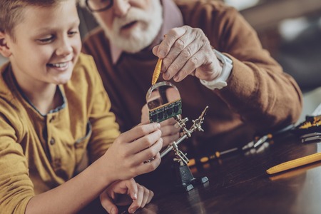 Technological progress. Pleased schoolboy expressing positivity while helping his grandfatherの写真素材