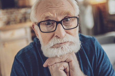 Facial expressions. Attentive bearded male person looking straight at camera and touching his chinの写真素材