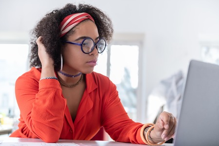 Observing her project. Bored good-looking African American lady working with laptop against and thinking about workloadの写真素材