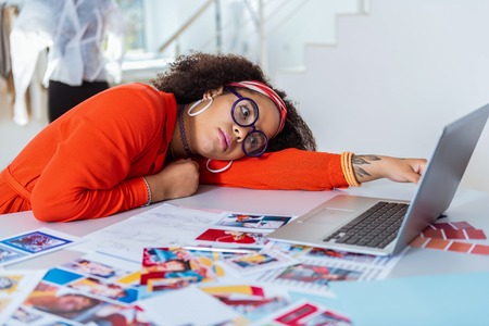 Young extravagant woman. Sad appealing exotic female lying on her working table with notebook right behindの写真素材