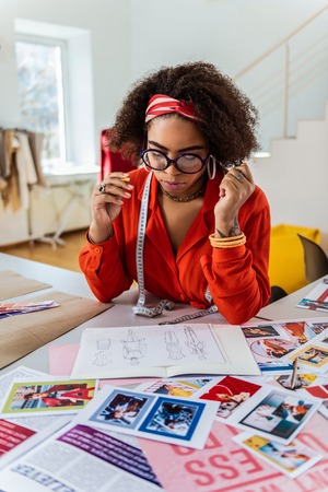 Dark-skinned lady thinking. Appealing bright lady working as designs creator and pondering about details of outfitsの写真素材
