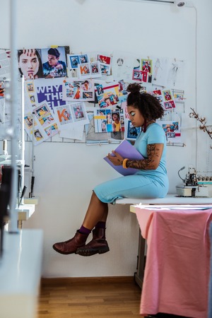 Seamstress filling diary. African American attractive lady matching her eyeshadow color with her blue dress while sittingの写真素材