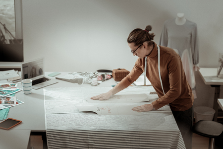 Cutting. Tall young professional designer wearing a brown garment getting ready for fabric cuttingの写真素材