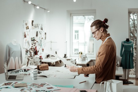 Designer at work. Fair-haired tall designer in a brown garment looking interested while working on a...