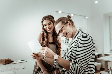 Good time together. Long-haired designer wearing eyeglasses and a pretty model laughing at the...