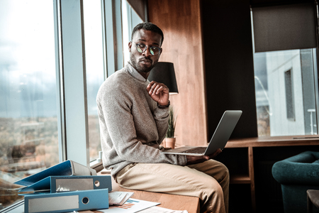 So serious. Handsome brunette man looking aside while holding laptop on right handの写真素材