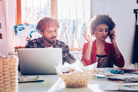 Bearded boyfriend. Bearded boyfriend with dreadlocks sitting near his woman speaking by phoneの写真素材