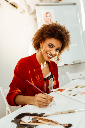 Curly student. Stylish curly dark-haired art student holding painting brush while drawingの写真素材