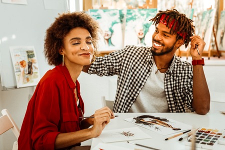 Loving man. Loving caring handsome man touching hair of his woman while painting togetherの写真素材