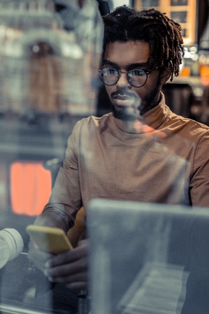 Be attentive. Handsome international man pressing lips while staring at screen of his gadget
