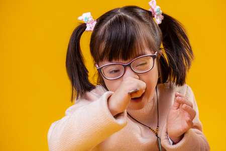 Cereals with milk. Extraordinary little girl with down syndrome having unusual face features eating meal with metal spoonの写真素材