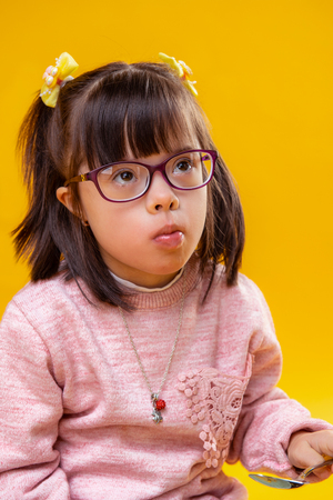 Eating snacks. Attentive little girl with brown eyes having down syndrome and funky dark hairstyleの写真素材