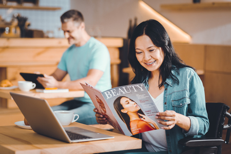 Pleasant time spending. Happy smiling woman reading a new magazine in a cafeの写真素材