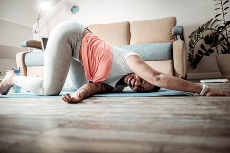 Weird meditative pose. Beaming smiling woman spending time in strange posture during yoga session