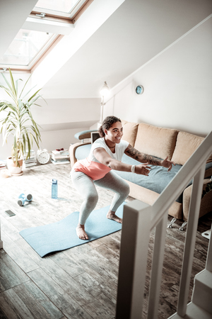 Pumping up legs. Cheerful young woman doing special exercises for fitting lower body and rising her handsの写真素材