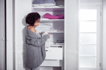 Wearing all grey. African American curly woman choosing clothes in her wardrobe and carrying white cozy sweaterの写真素材
