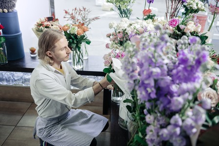 Soft colors. Concentrated male person wearing apron while working in floral shop