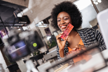 Good mood. Beautiful dark-skinned makeup blogger in an orange top feeling stunning while making a post to the blogの写真素材