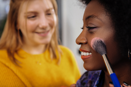 Nice day. Cute beaming dark-skinned model with coral lipstick looking contented while trying on a new blusher swatchの写真素材